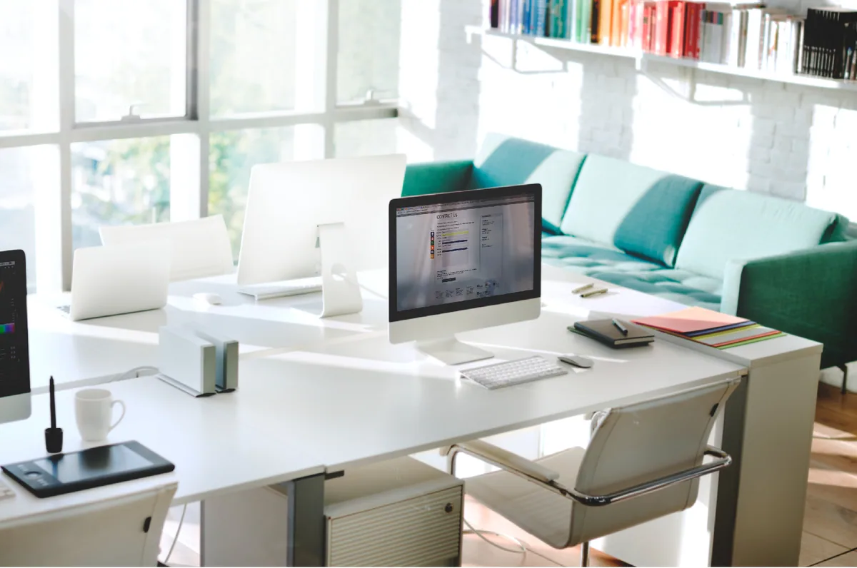 A bright office with white desks and a green sofa